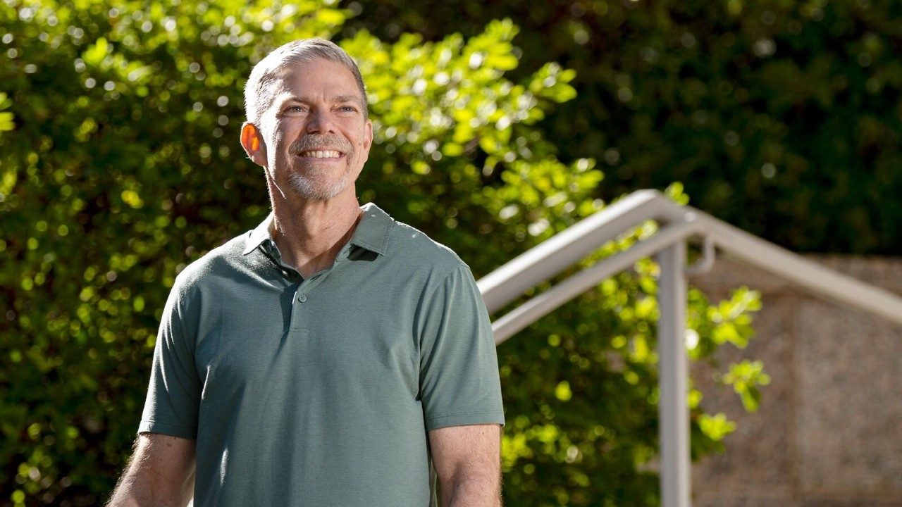 A man in a green short sleeve polo shirt smiling while standing outside on a staircase