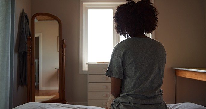 Woman sitting on a bed alone in her bedroom