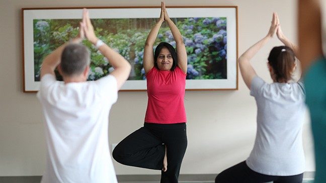 Yoga therapist Smitha Mallaiah stands in tree pose as she leads two students in yoga class.