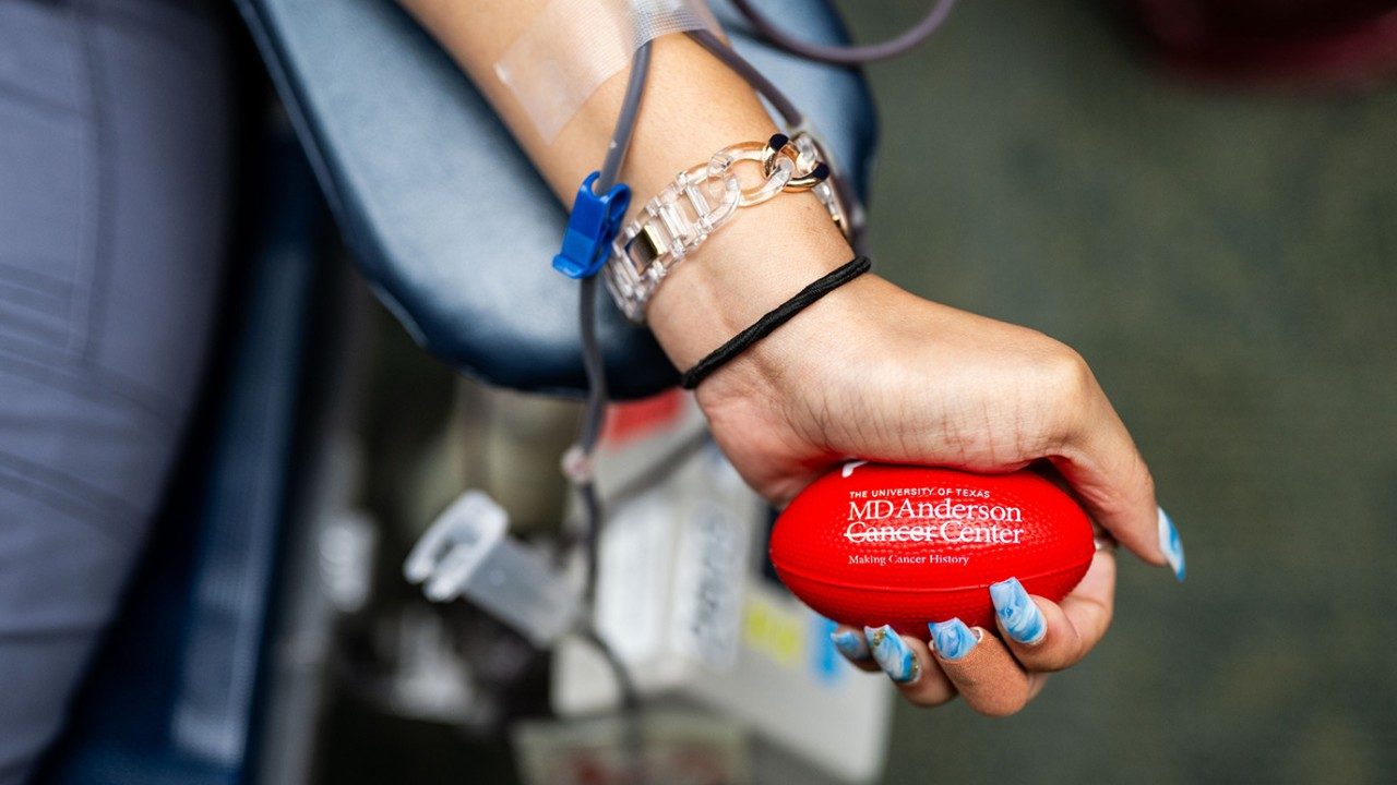 Close-up of manicured hand squeezing bright red MD Anderson-branded stress ball during blood donation