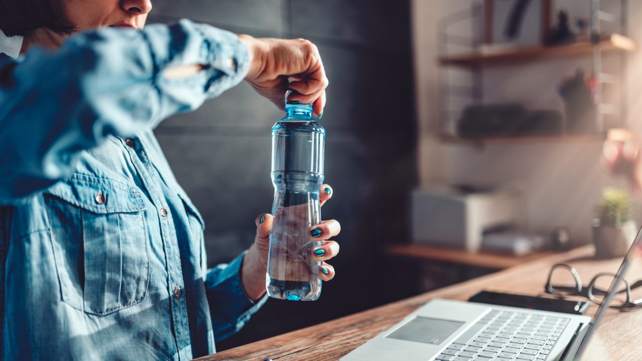 Woman at desk opens bottle of water