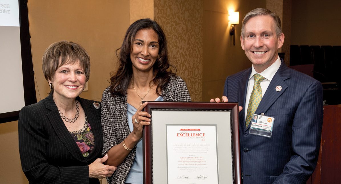 Padmanee Sharma, M.D., Ph.D. holds a framed certificate noting her $15,000 award as she poses with Regina Rogers and Peter WT Pisters, M.D.